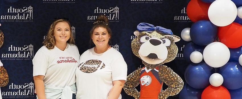 Two alumni members wearing South shirts standing next to Ms. Pawla cutout.